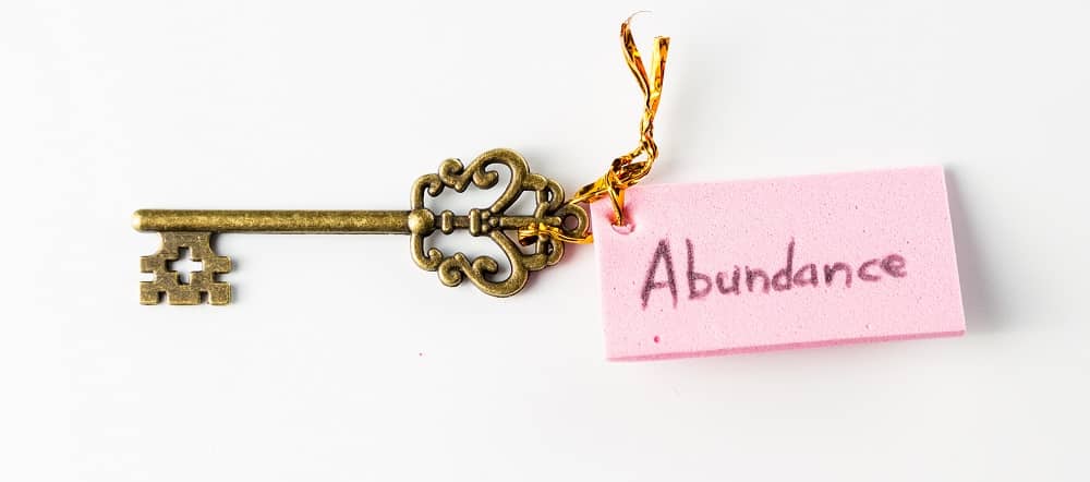 Close up of an ornamental key with the word abundance hand written on a pink tag isolated on a white background